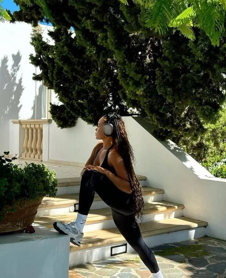 Image of Black Woman Stretching Before Run in Gorgeous Mediterranean Neighborhood with Headphones and New Balance Sneakers
