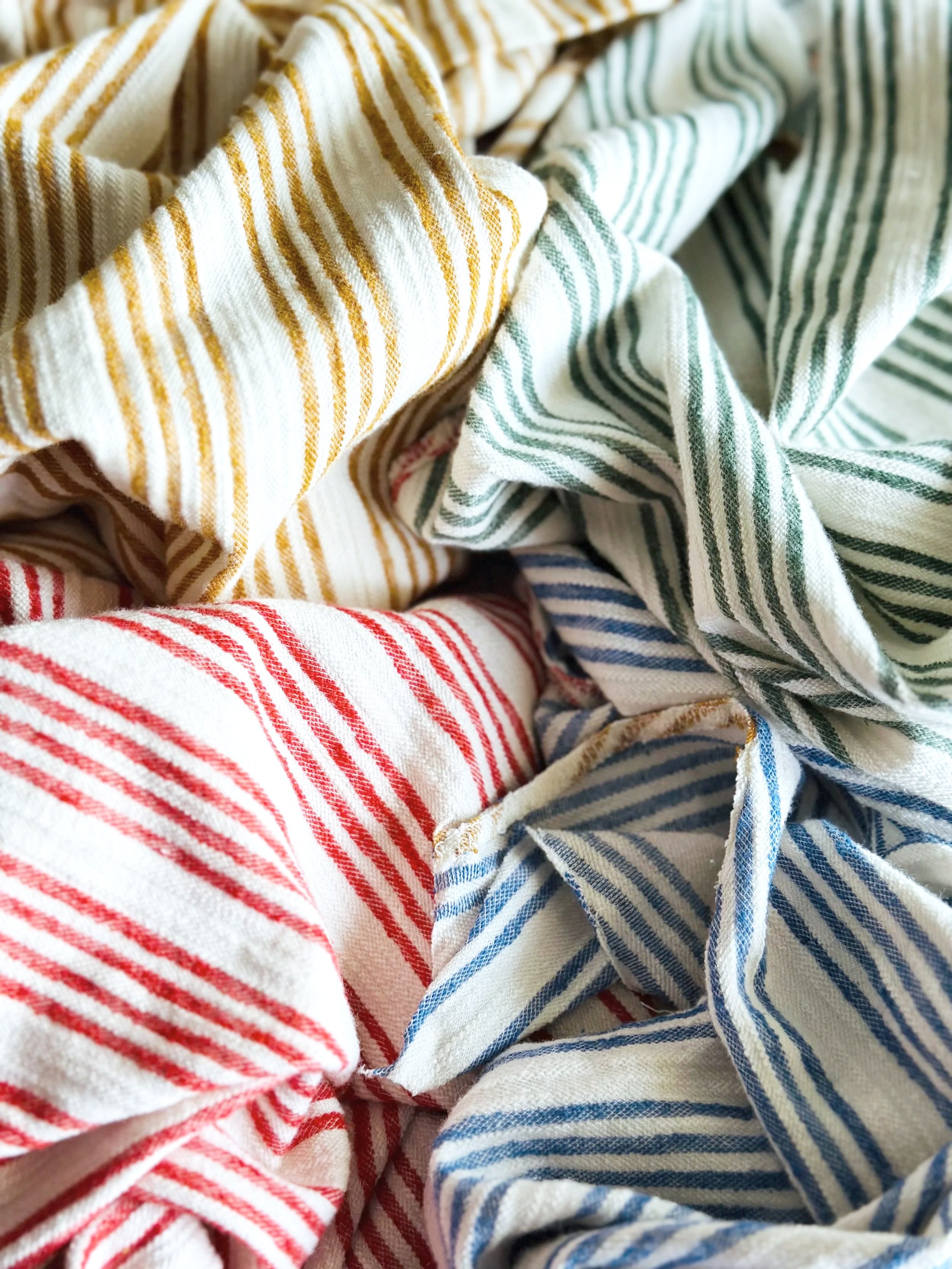  Four colors of striped linen from one thrifted dress — mustard, red, blue, and green — waiting to become handmade bags and pouches 