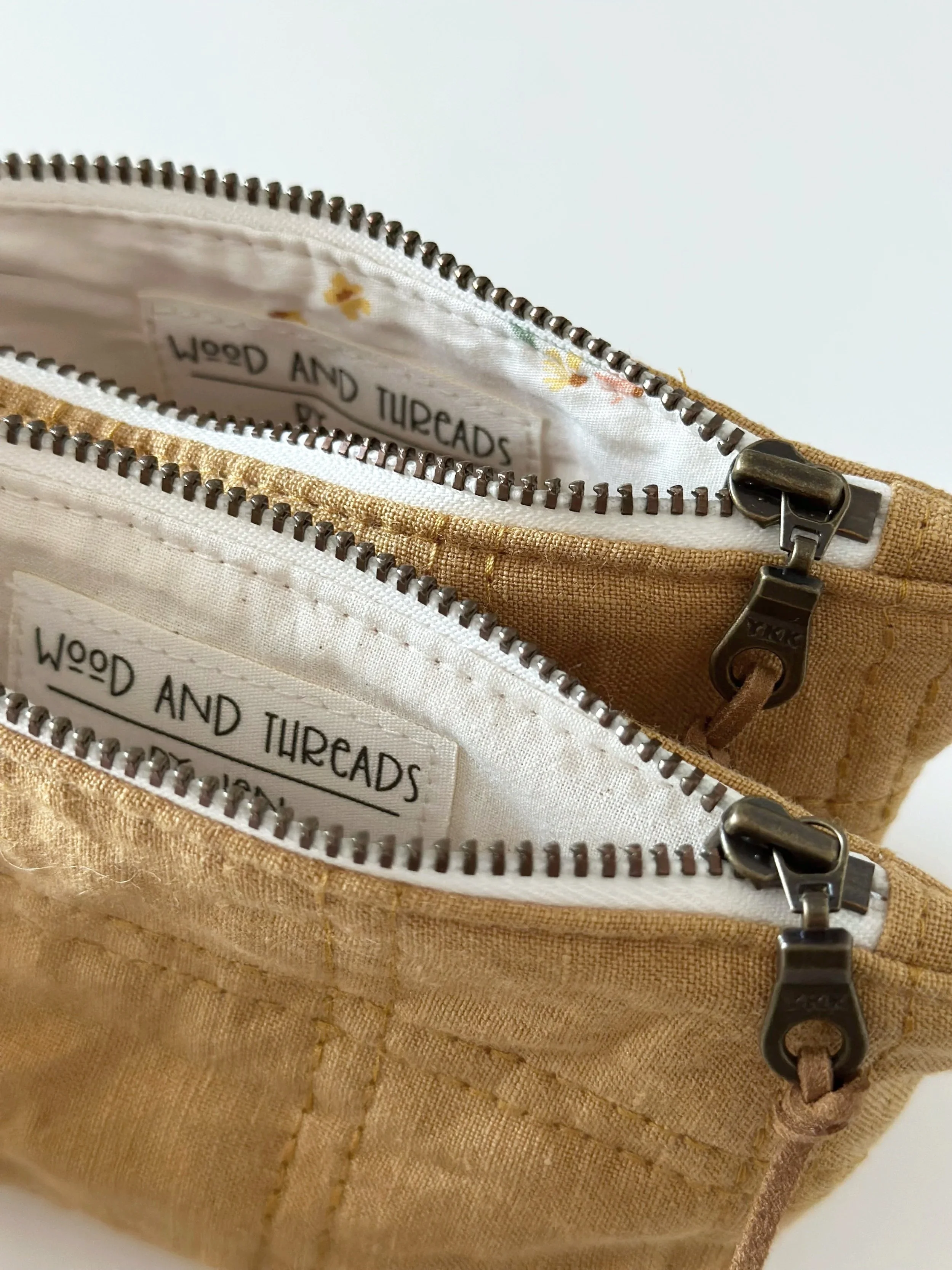 Close up of two open cornfield yellow quilted linen pouches showing white floral printed lining, brass zippers, and Wood and Threads by Jen fabric labels
