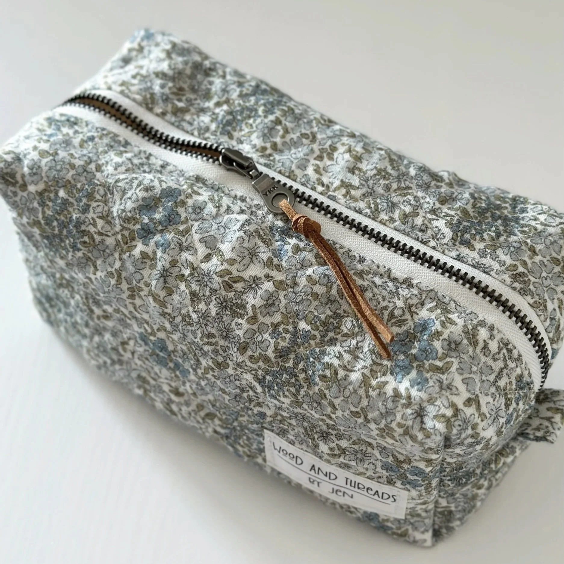 Top view of green crosshatch boxy pouch with metal zipper and suede pull