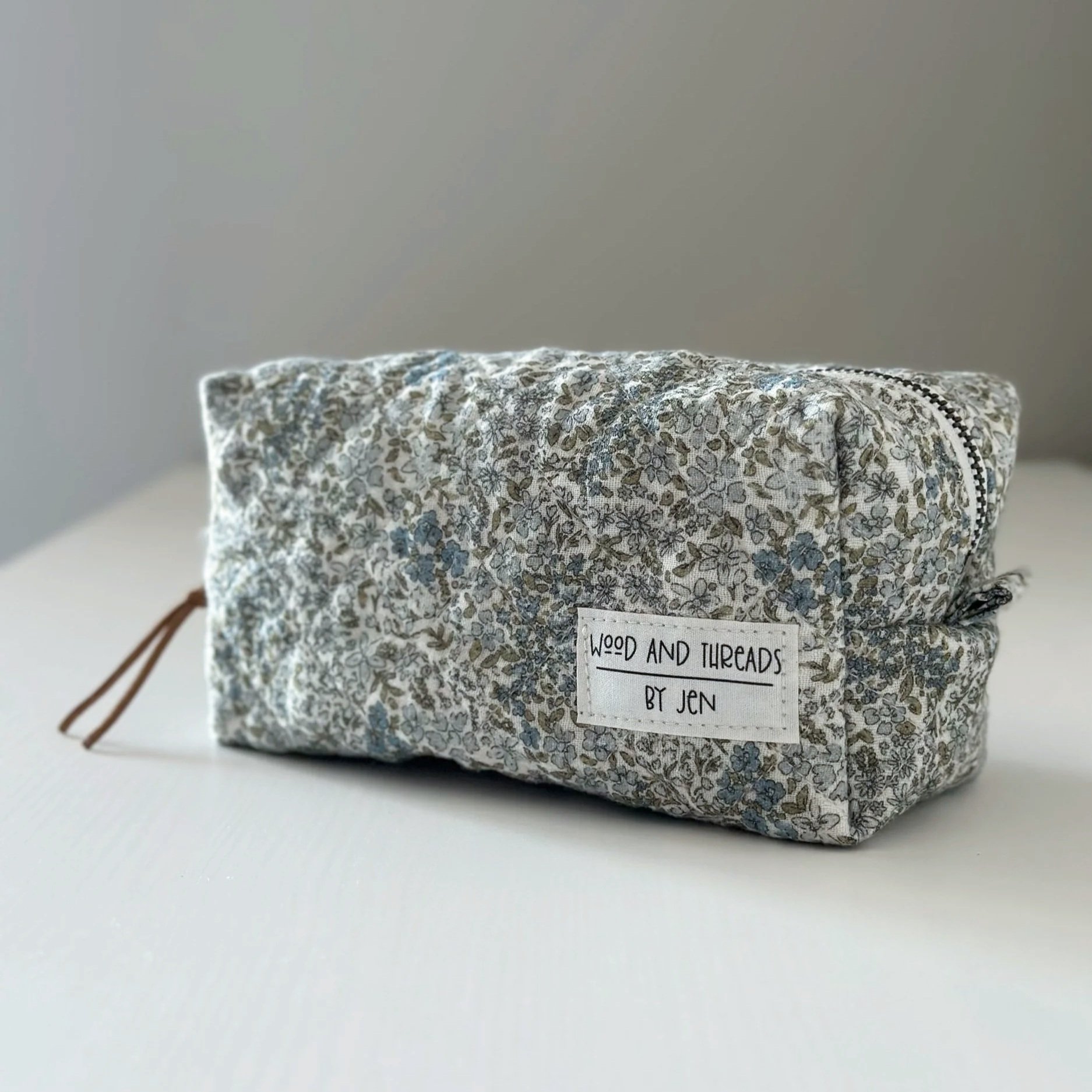 Green crosshatch quilted boxy pouch with brand tag, angled view