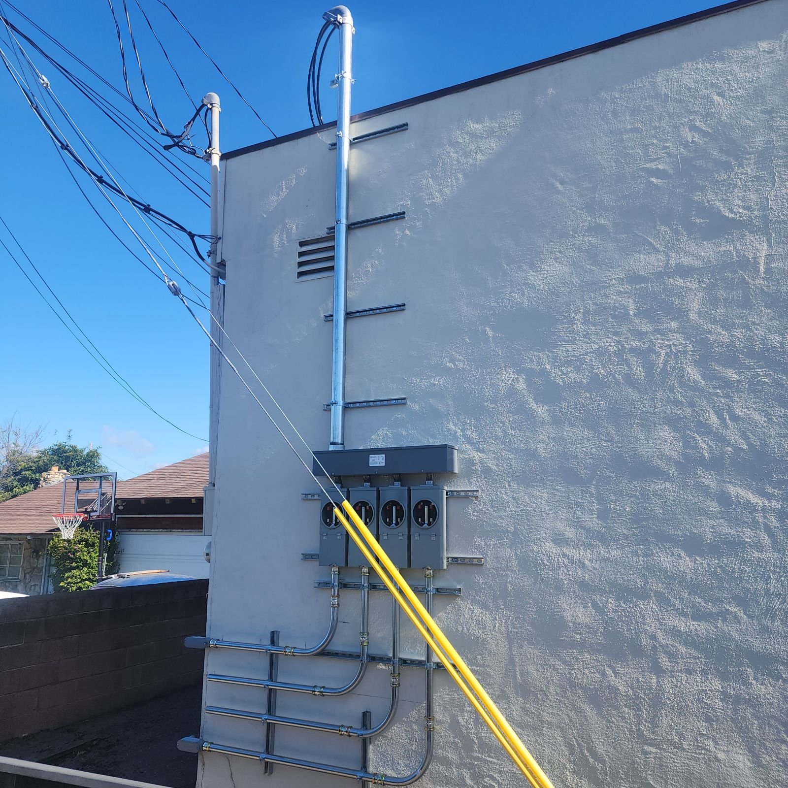 Electric meters and wiring on the exterior of a building with a basketball hoop visible in the background.