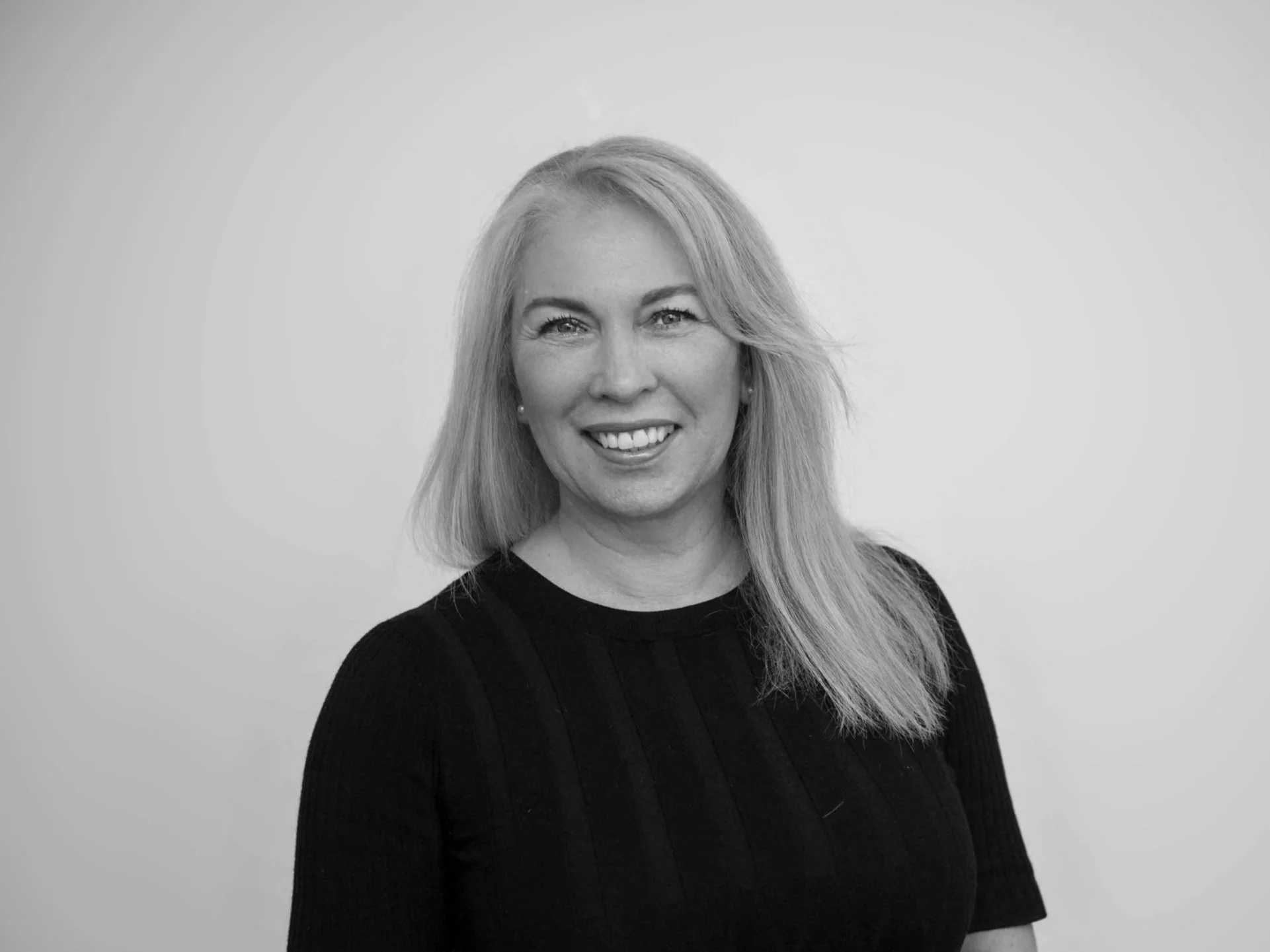 Black and white portrait of a smiling woman with shoulder-length hair, wearing a black top, against a plain light background.