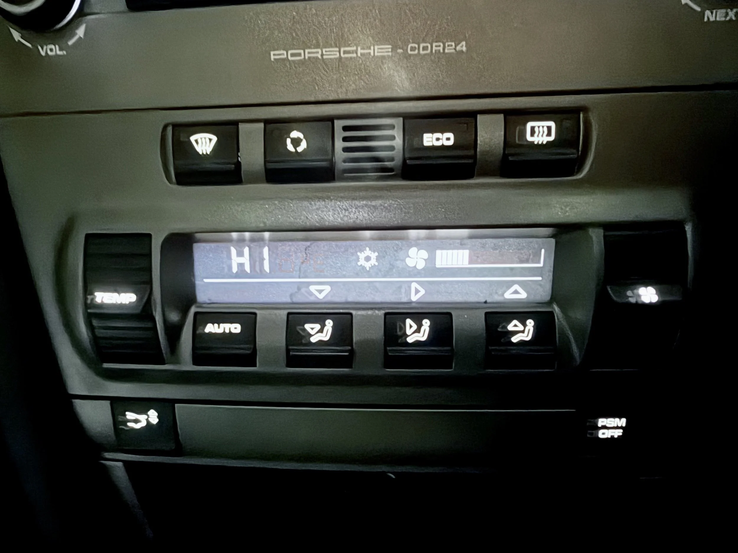 Close-up of a car's dashboard with buttons for defrosting, recycling, eco mode, and heated seats, and a digital display showing temperature and fan speed controls.
