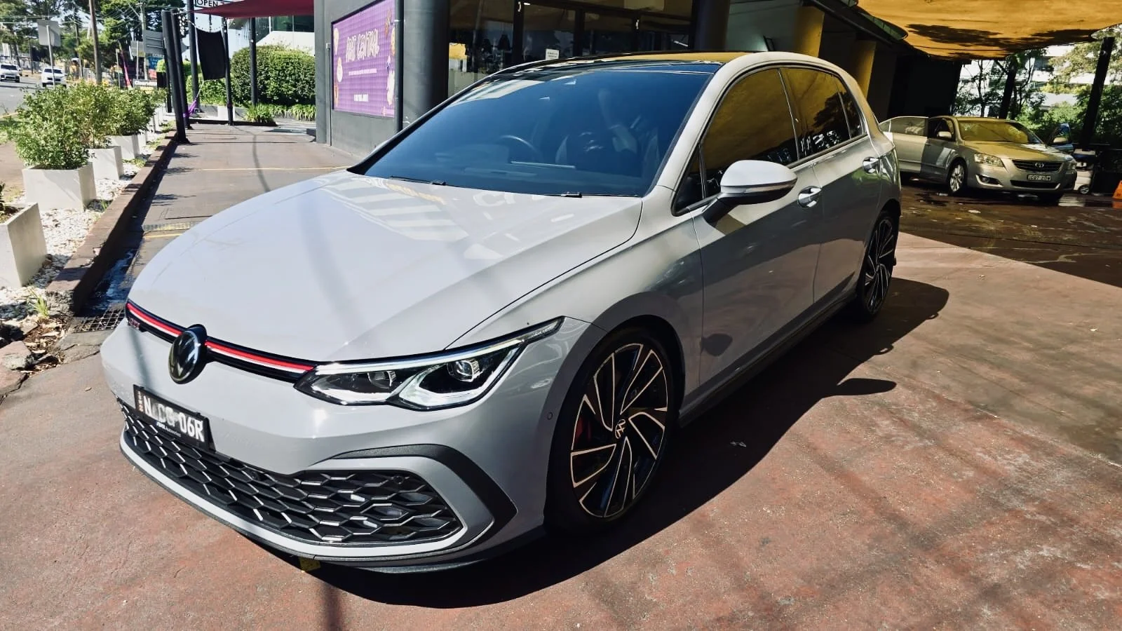 A silver Volkswagen car parked outside a building with other vehicles in the background during daytime.