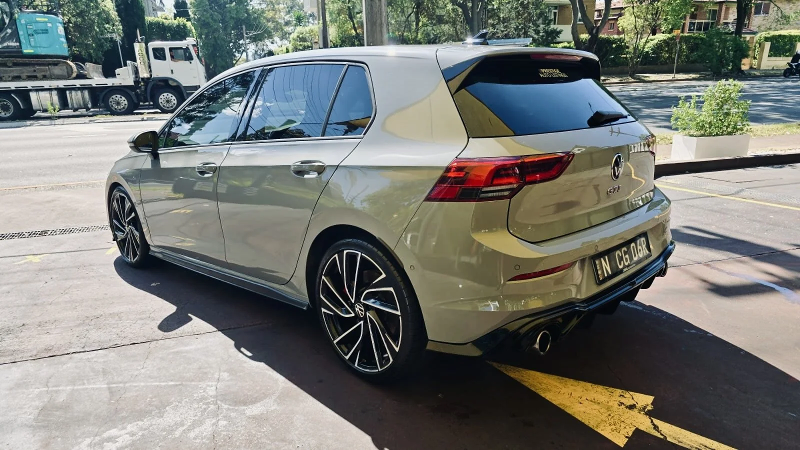 Gray Volkswagen Golf GTI hatchback parked in a parking lot with buildings and trees in the background.
