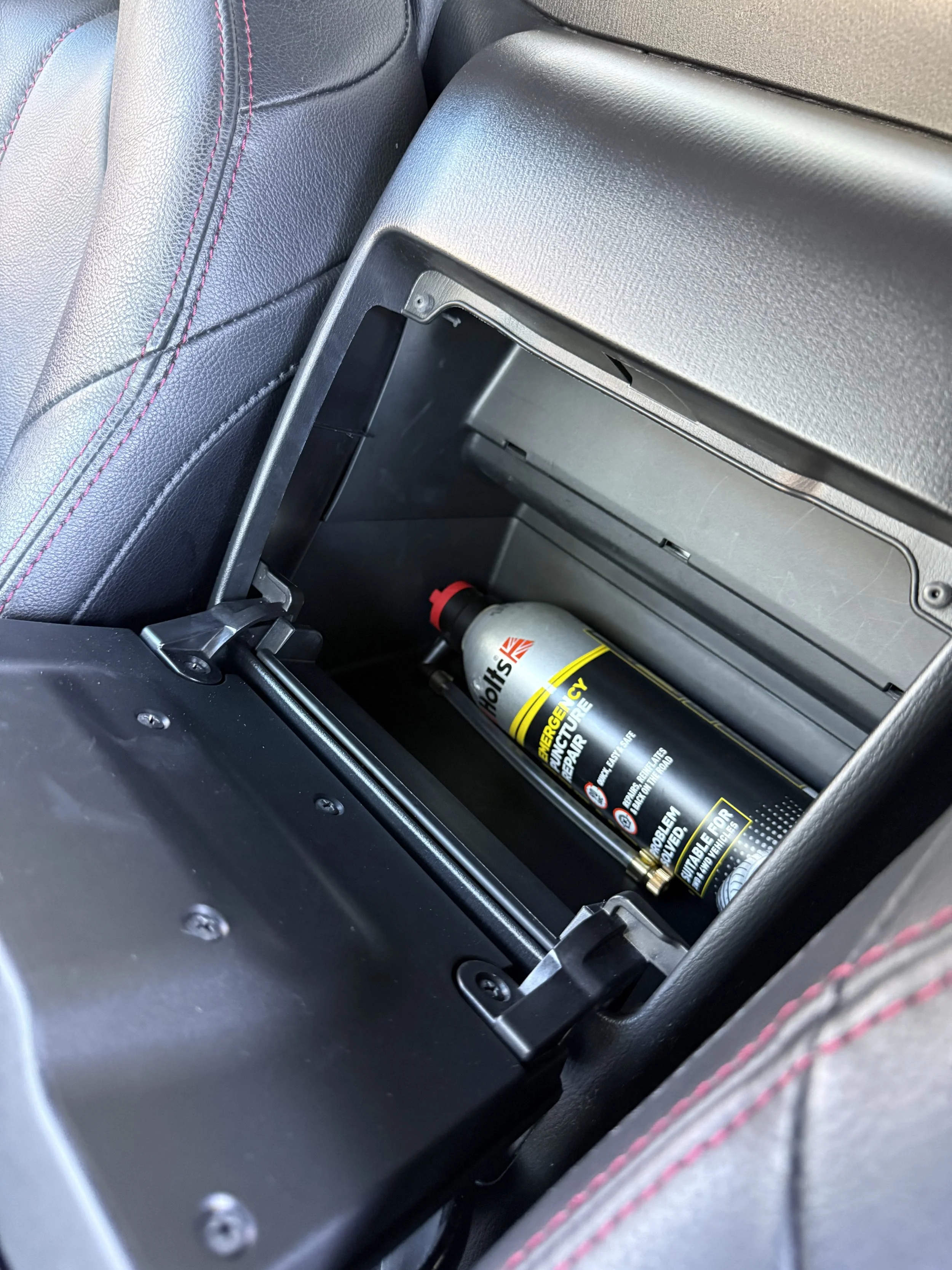 Car trunk with a bottle of Häagen-Dazs ice cream and empty storage compartment.