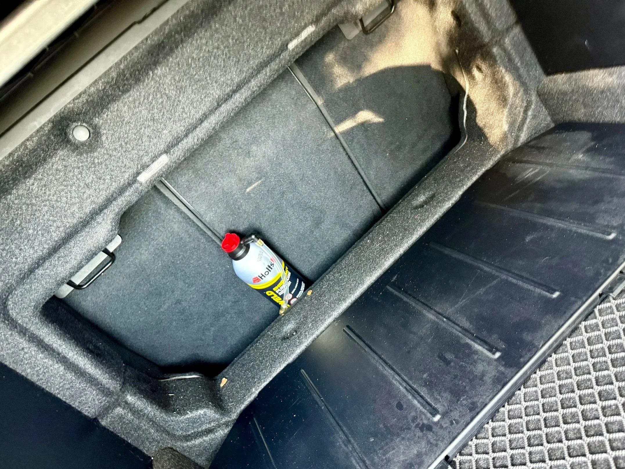 Car trunk with a bottle of Häagen-Dazs ice cream and empty storage compartment.