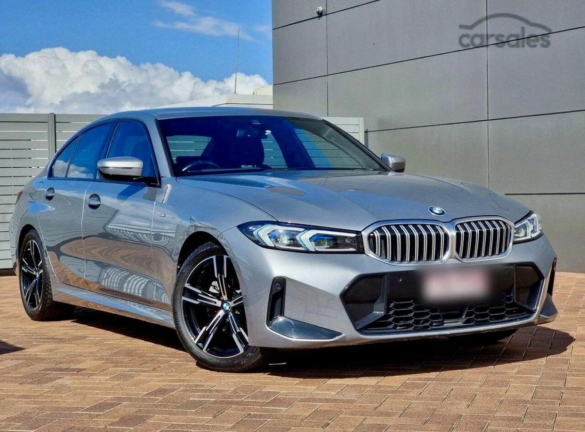 A silver BMW sedan parked on a brick surface outside a building with the Corsalets logo. The car features a kidney grille, modern LED headlights, and sporty black and silver wheels.