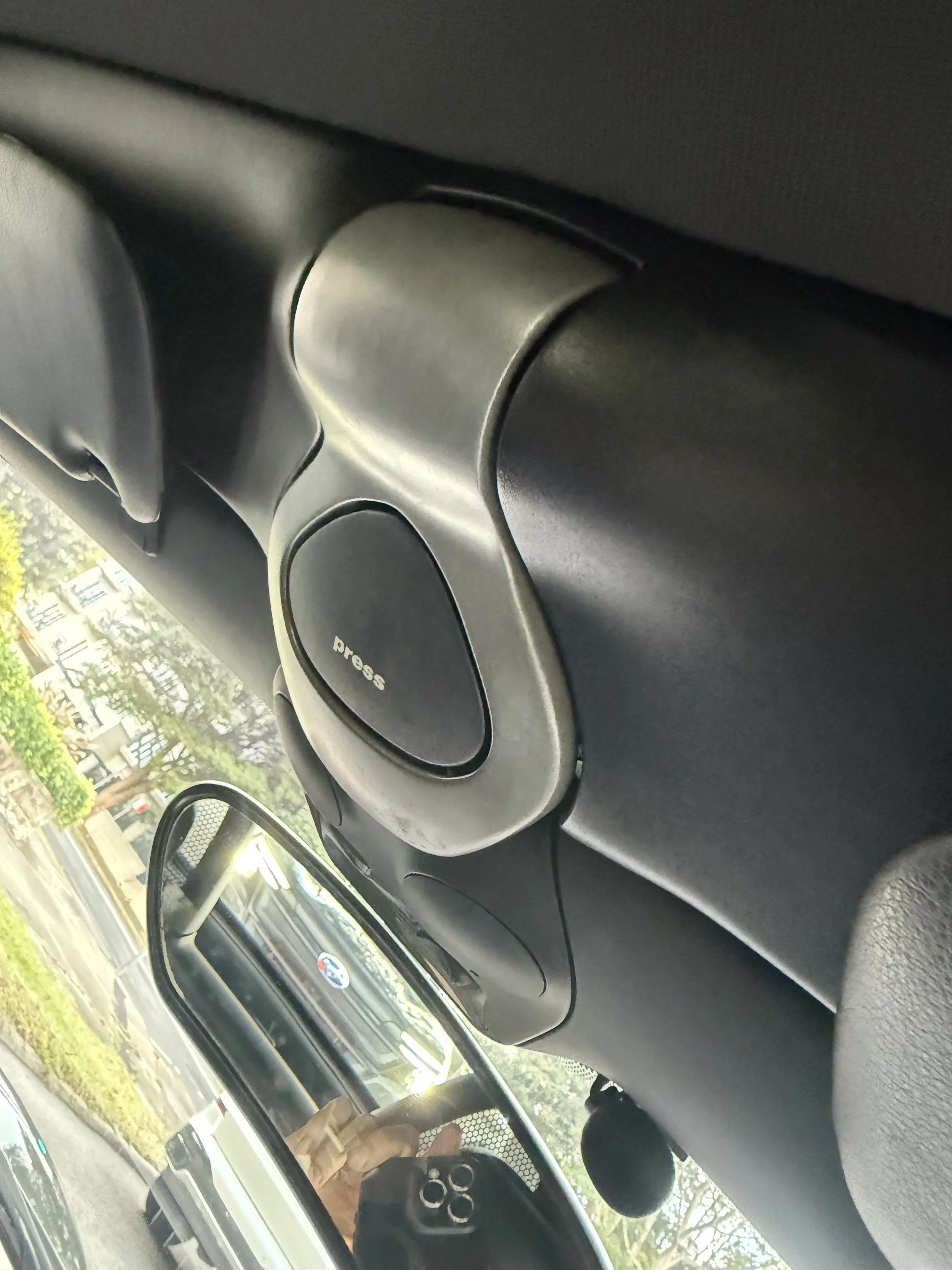 The trunk of a car with a black carpeted surface, showing a small storage compartment with a warning label and a black netted organizer, and part of the car's internal structure.