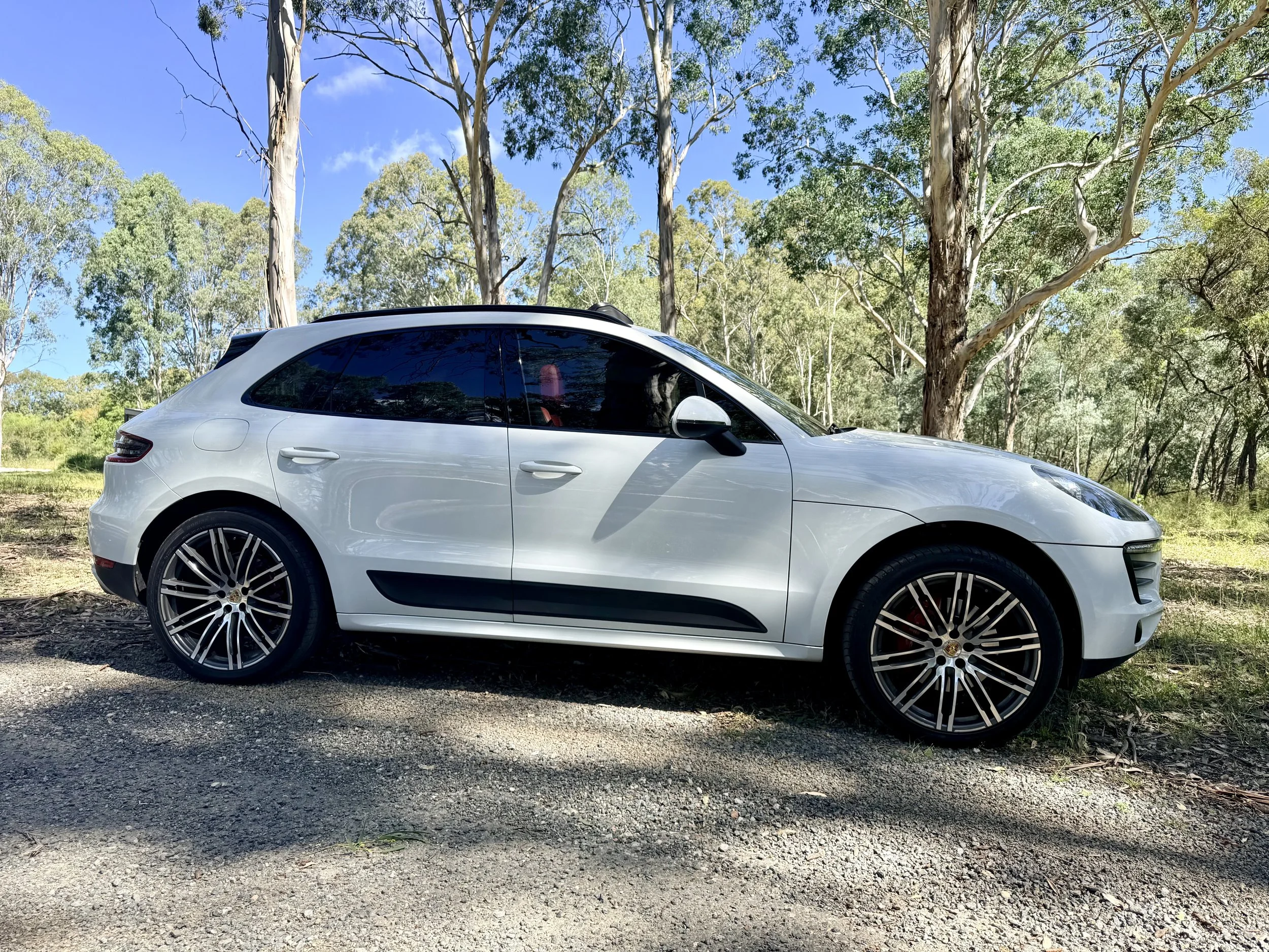 White SUV parked on street in front of a white wall and house with arched windows, palm trees, and clear blue sky