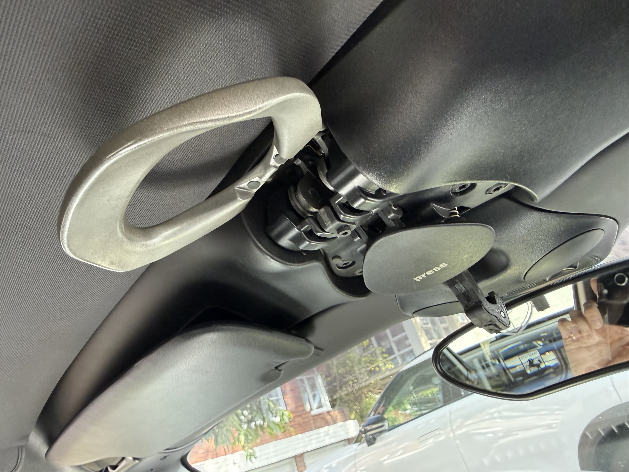 The trunk of a car with a black carpeted surface, showing a small storage compartment with a warning label and a black netted organizer, and part of the car's internal structure.