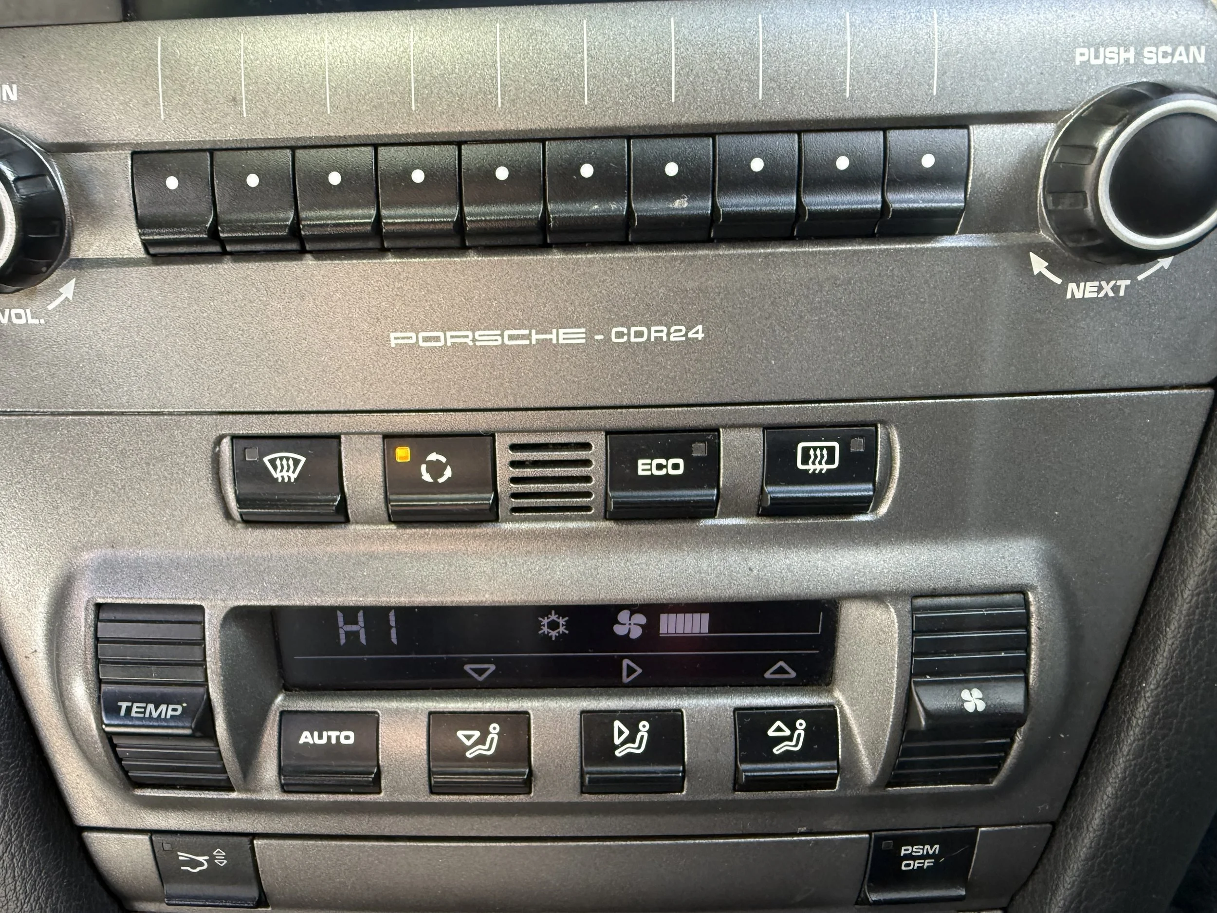 Close-up of a car's dashboard with buttons for defrosting, recycling, eco mode, and heated seats, and a digital display showing temperature and fan speed controls.