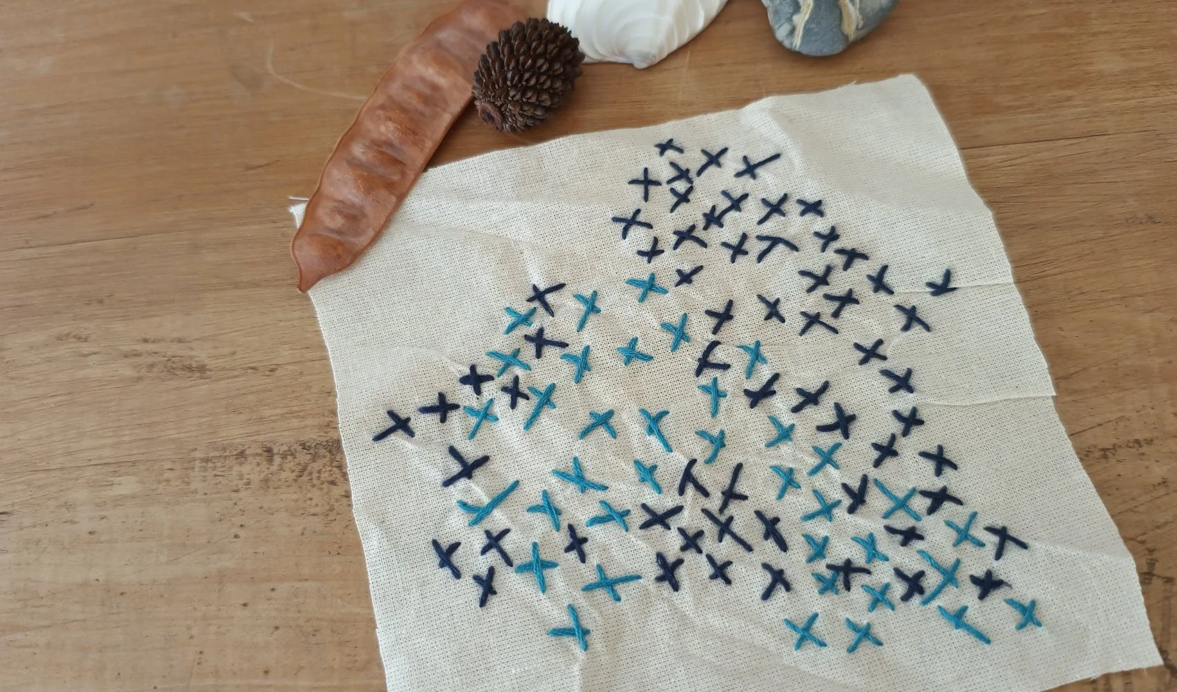 A square piece of white cotton with irregular cross stitching in two shades of blue as part of the Menindee Memorial Loop Project by Julie Paterson