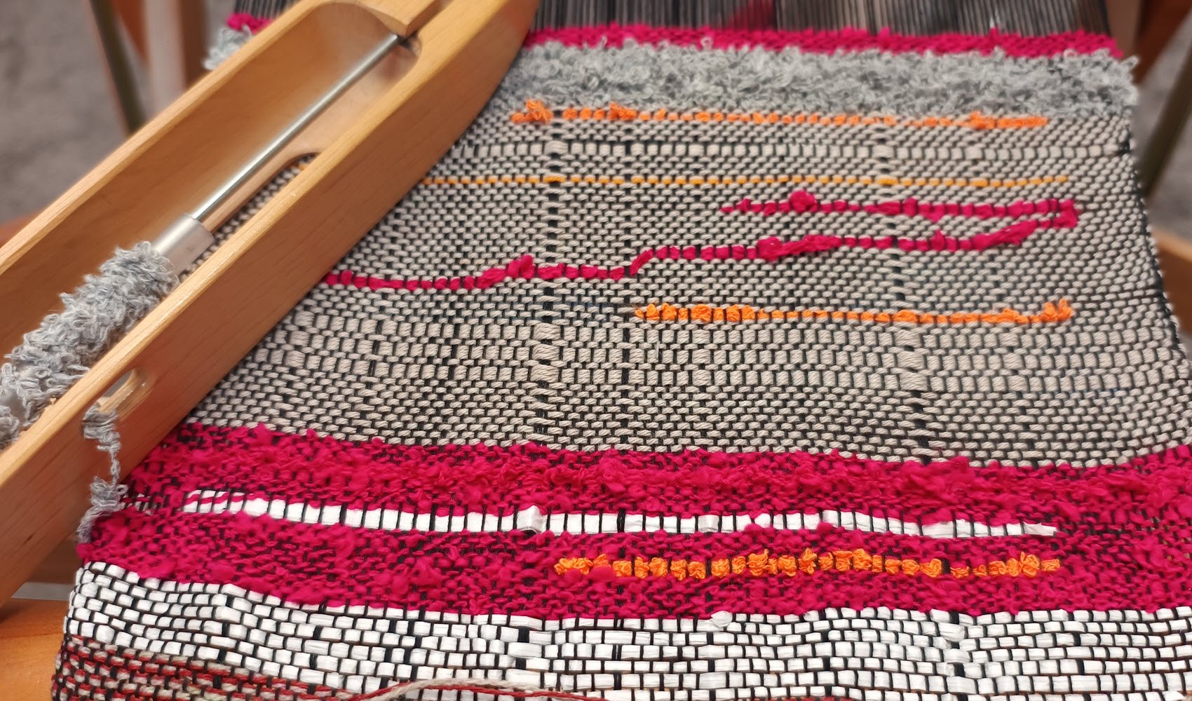 A close-up of a Saori woven cloth made of yarn in natural shades with some bright pink and orange woven into it.