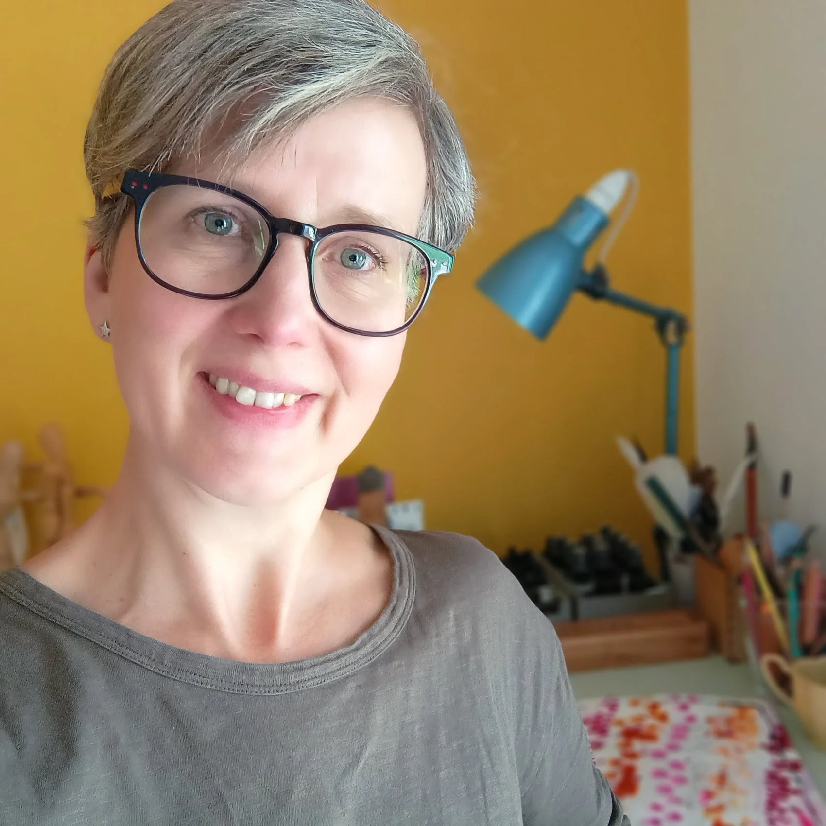 Arts-based and trauma-informed coach Conny Weyrich in her studio in front of her yellow wall