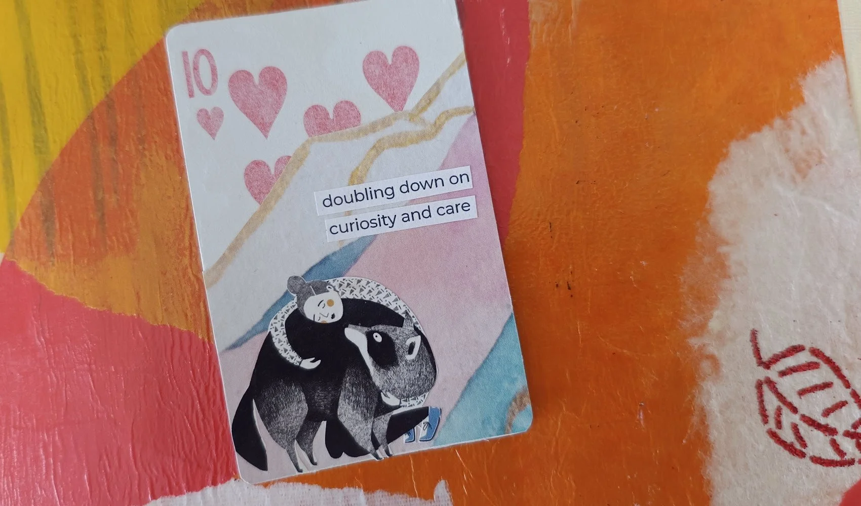 An altered playing card with an illustration of a girl hugging a bear and the words 'doubling down on curiosity and care'