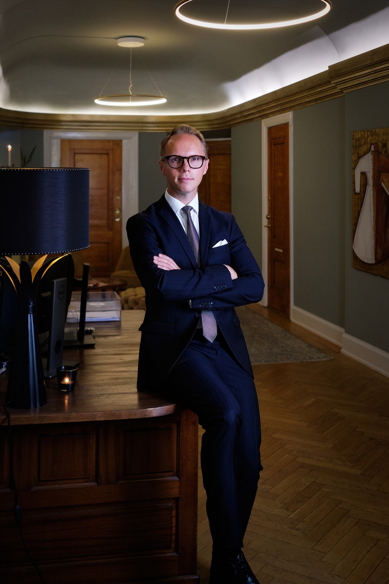 Full body portrait of a man sitting on a desk in a professional setting.