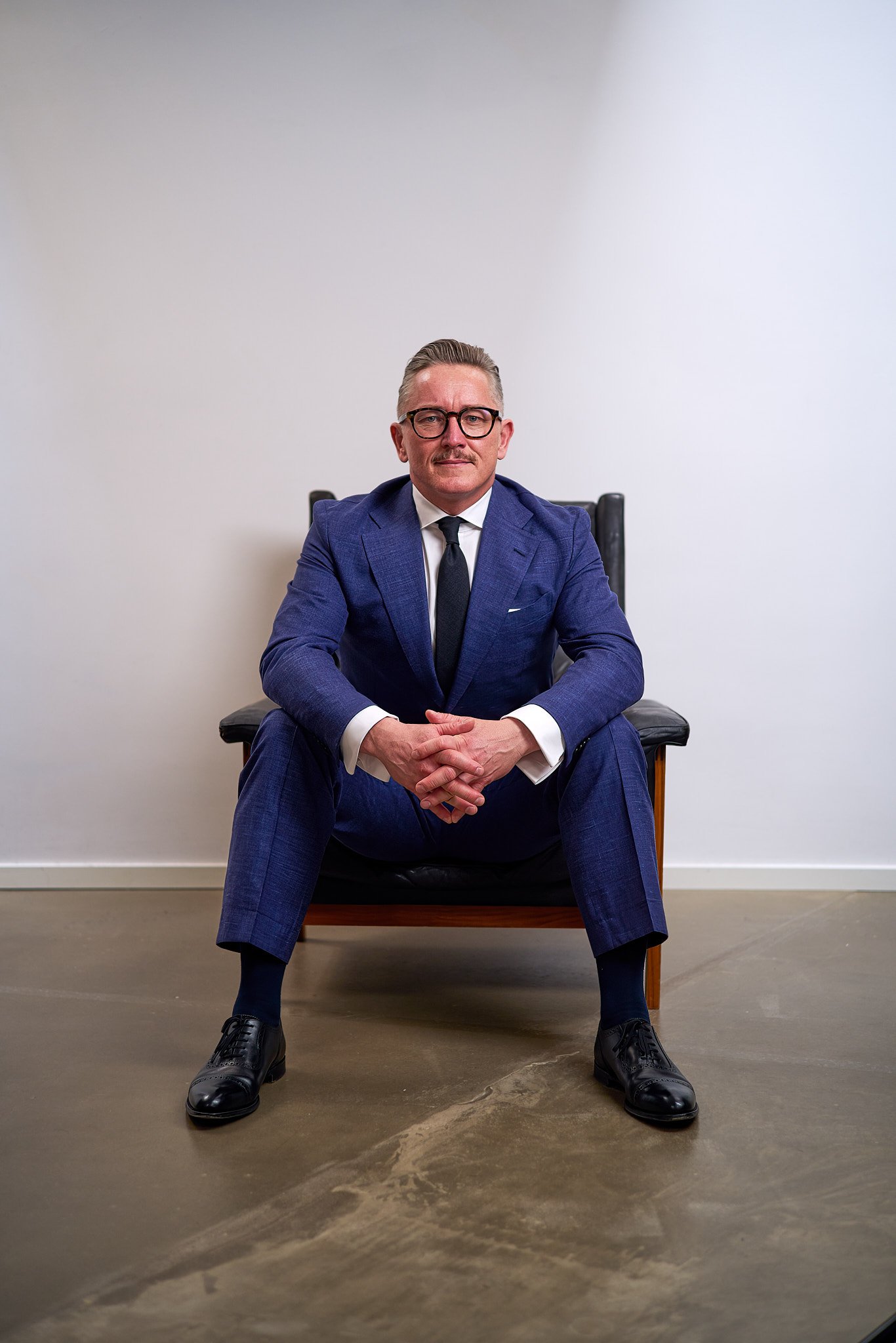 Business portrait of a man sitting in a chair with folded hands.