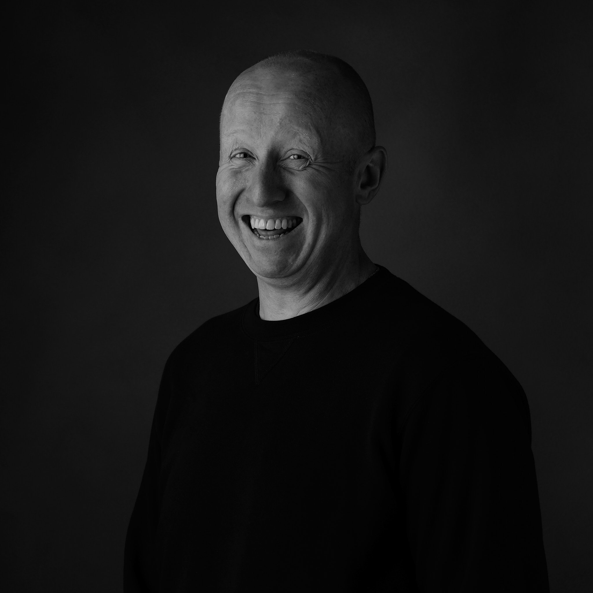 A black and white portrait of a bald man with a big smile.