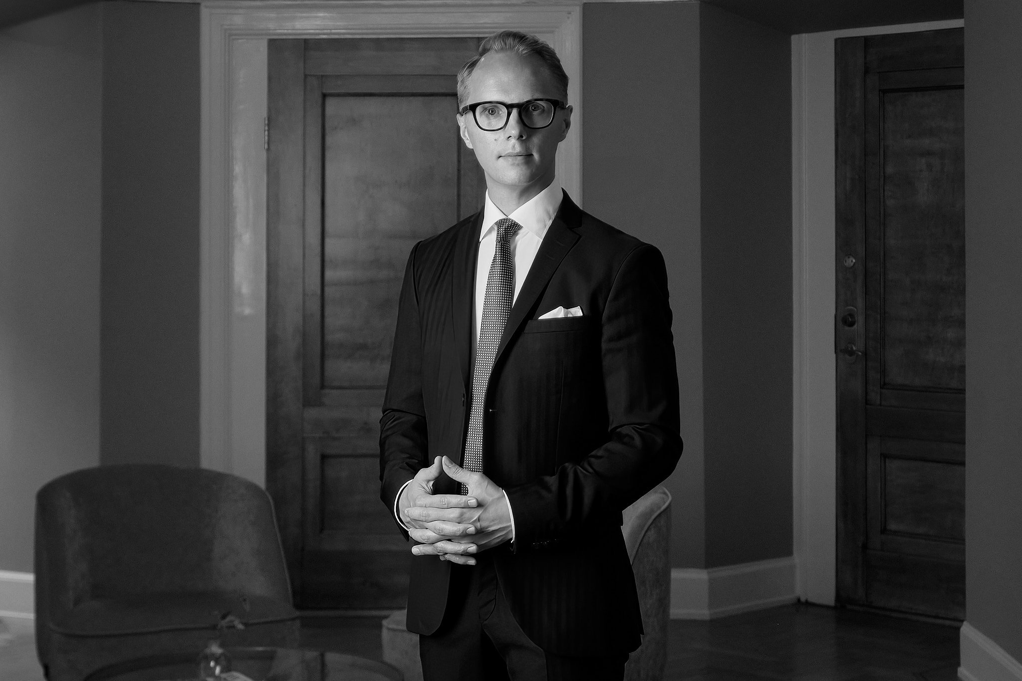 Black and white business portrait of a man in a suit with folded hands.