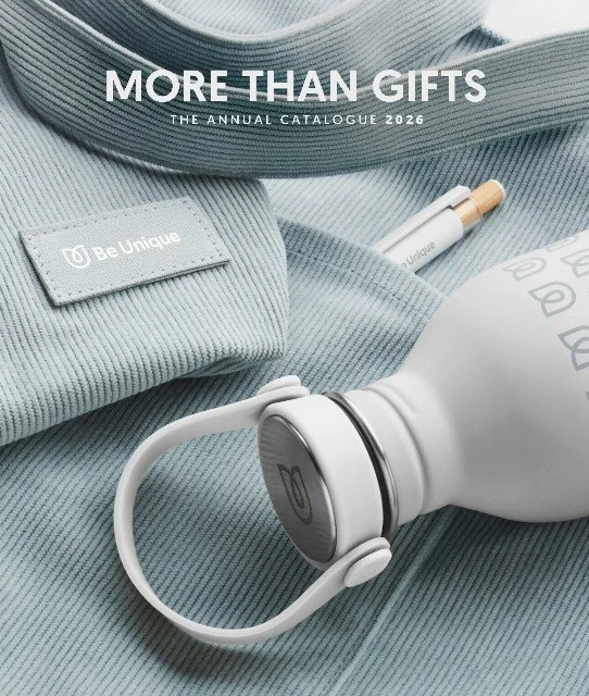 Kuvaus tuotteista ja tekstiä, jossa lukee "More Than Gifts, The Annual Catalogue 2026" ja "Be Unique". Esillä ovat muki ja kynä, jotka ovat osana lahjatavaroiden katalogia.