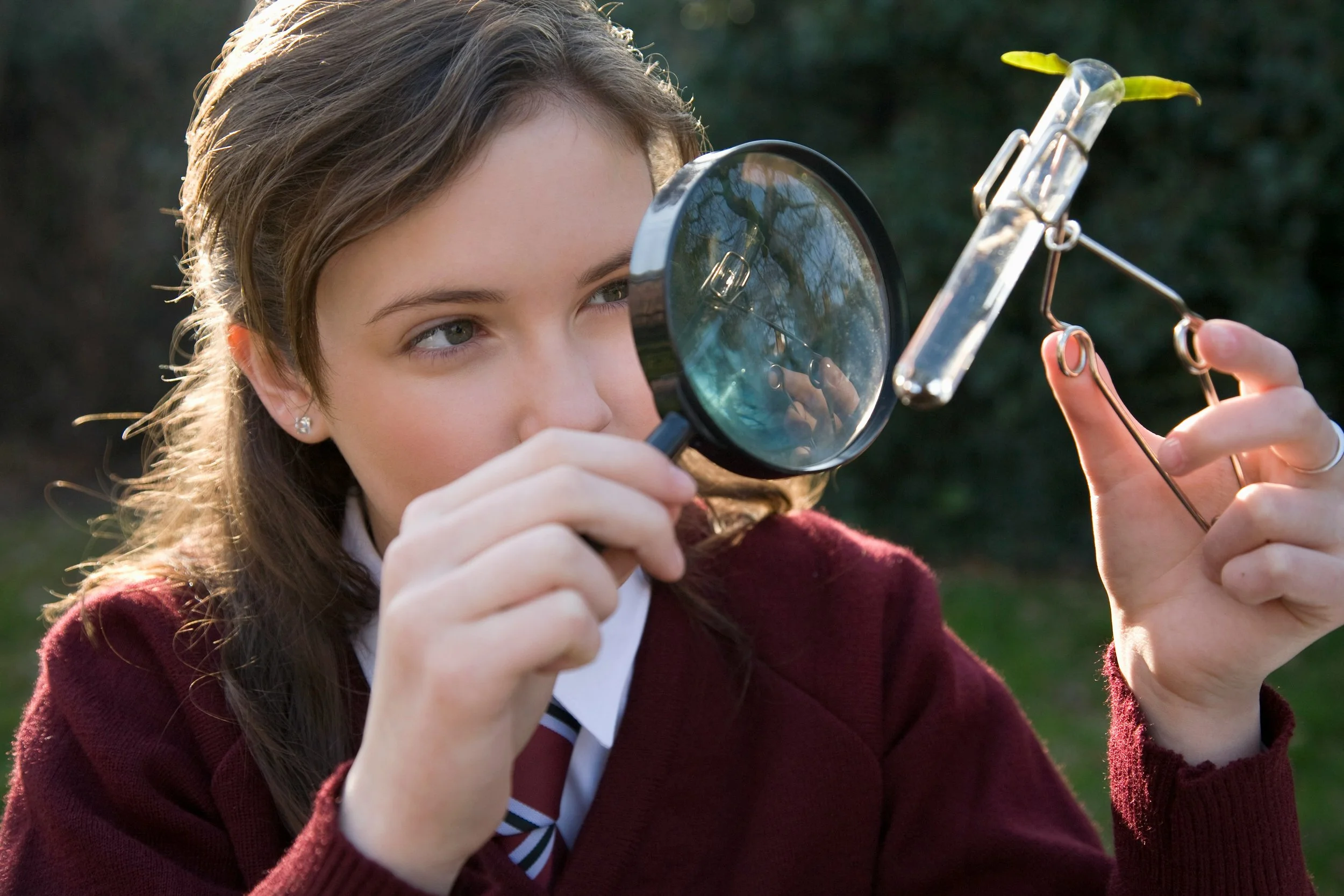 female student using a microscope to look at a test tube containing plant material