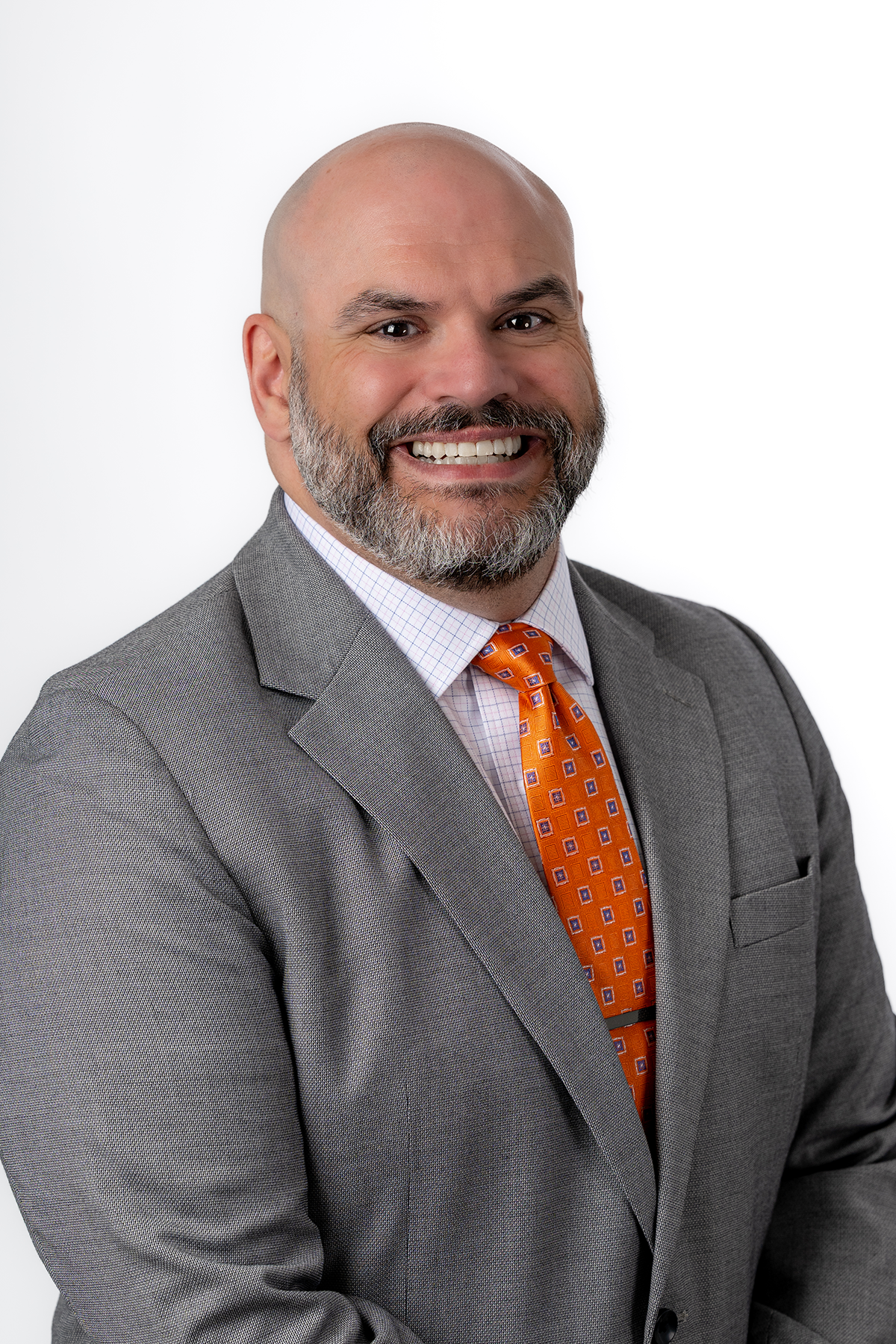 Man in a gray suit with a checked shirt and an orange patterned tie, smiling, in a professional headshot against a white background.