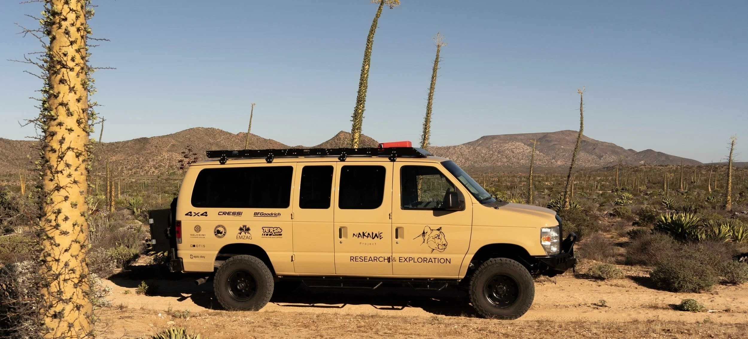 Baja Adventures vehicle parked in a desert with cacti and mountains in the background in Baja California