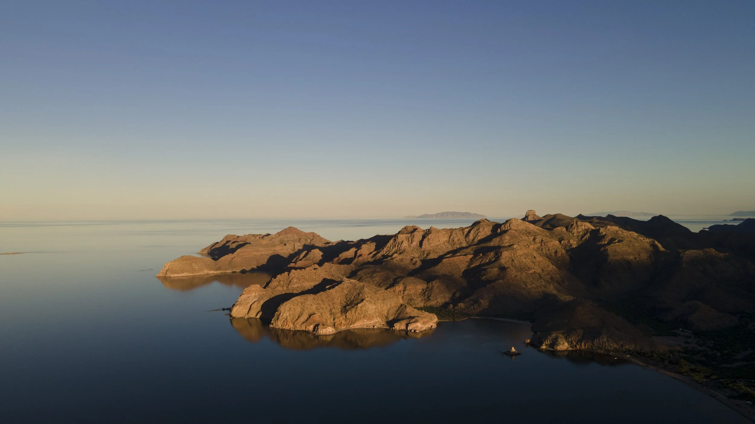 Rocky mountains during sunset or sunrise, with a clear sky and calm waters reflecting the landscape, in Loreto, Baja California Sur, Mexico