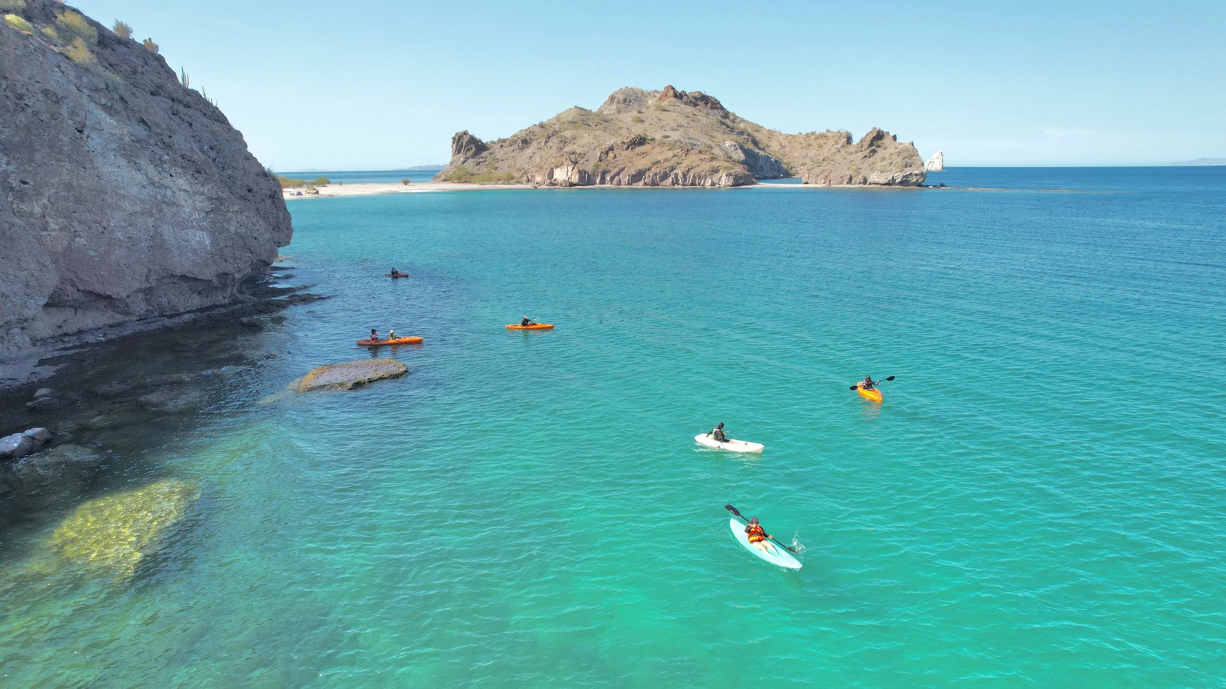 People kayaking on turquoise water near a rocky coastline  in Loreto, Baja California Sur, Mexico