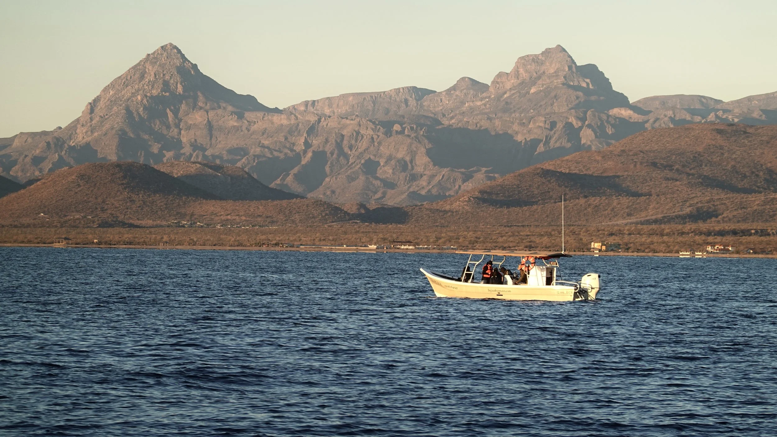 A small white boat on calm water with mountains in the background during sunset or sunrise.