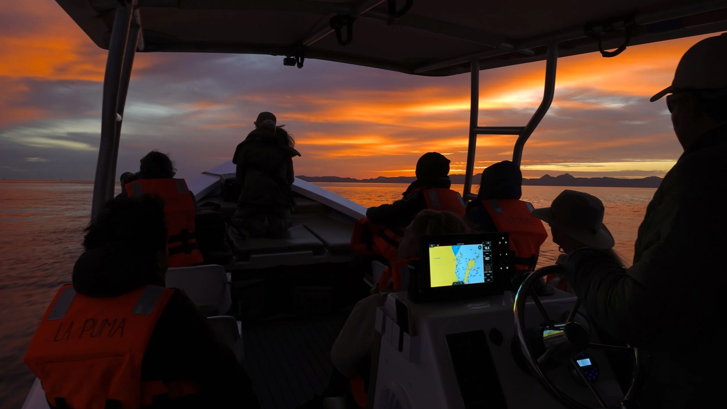 People on Baja Adventures boat during sunset, with the sky filled with orange, yellow, and purple hues, in Loreto Bay National Park during an marine adventure.