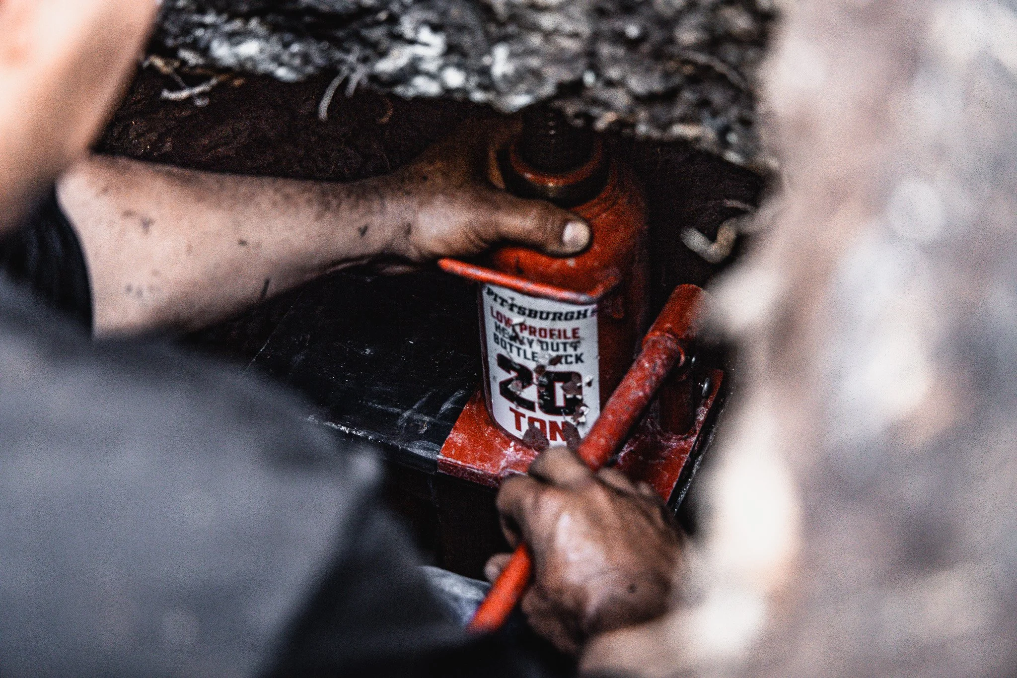 Person using a red 20-ton bottle jack under a vehicle or structure.