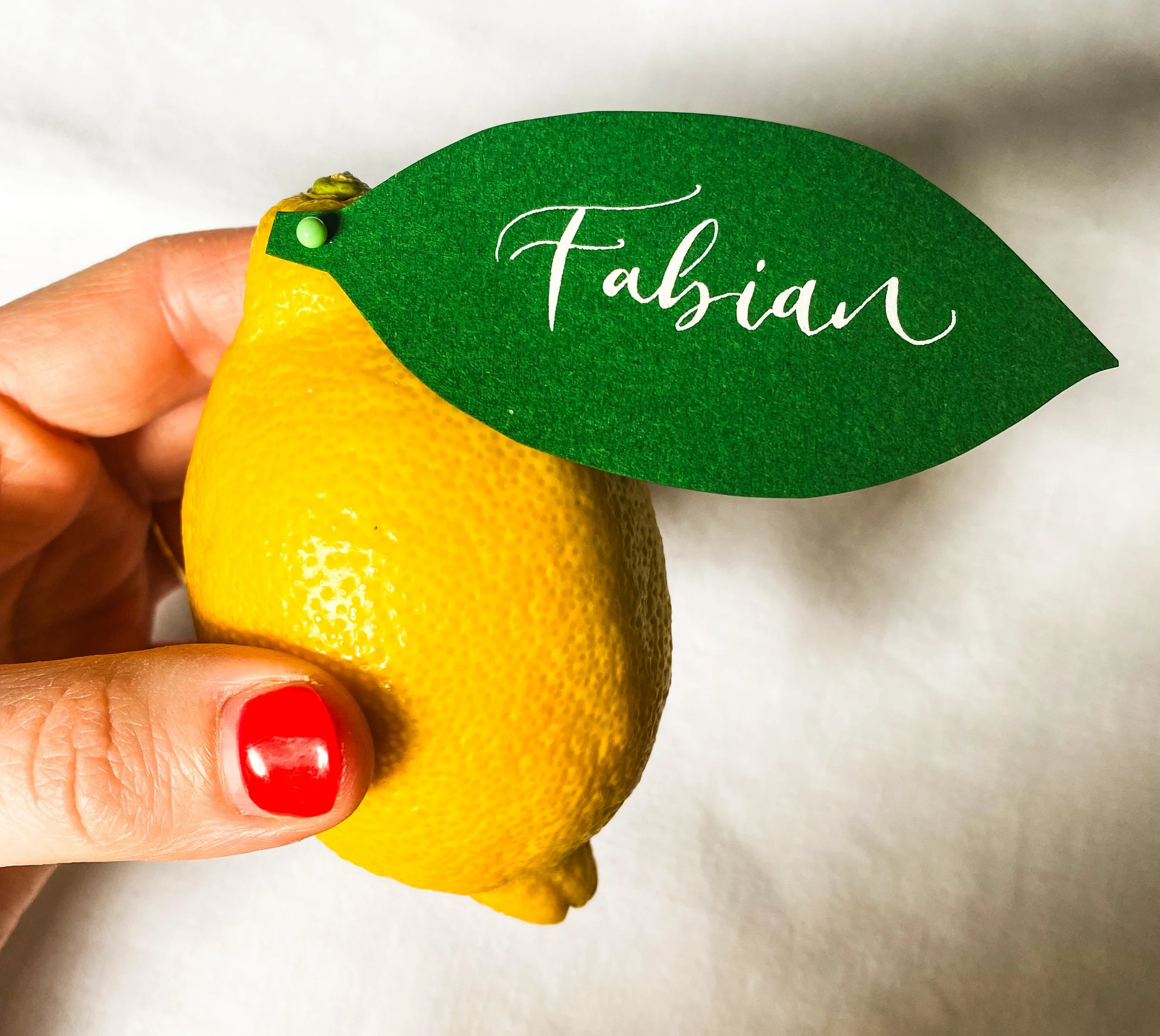 A calligraphy placecard shaped like a leaf, attached to a lemon