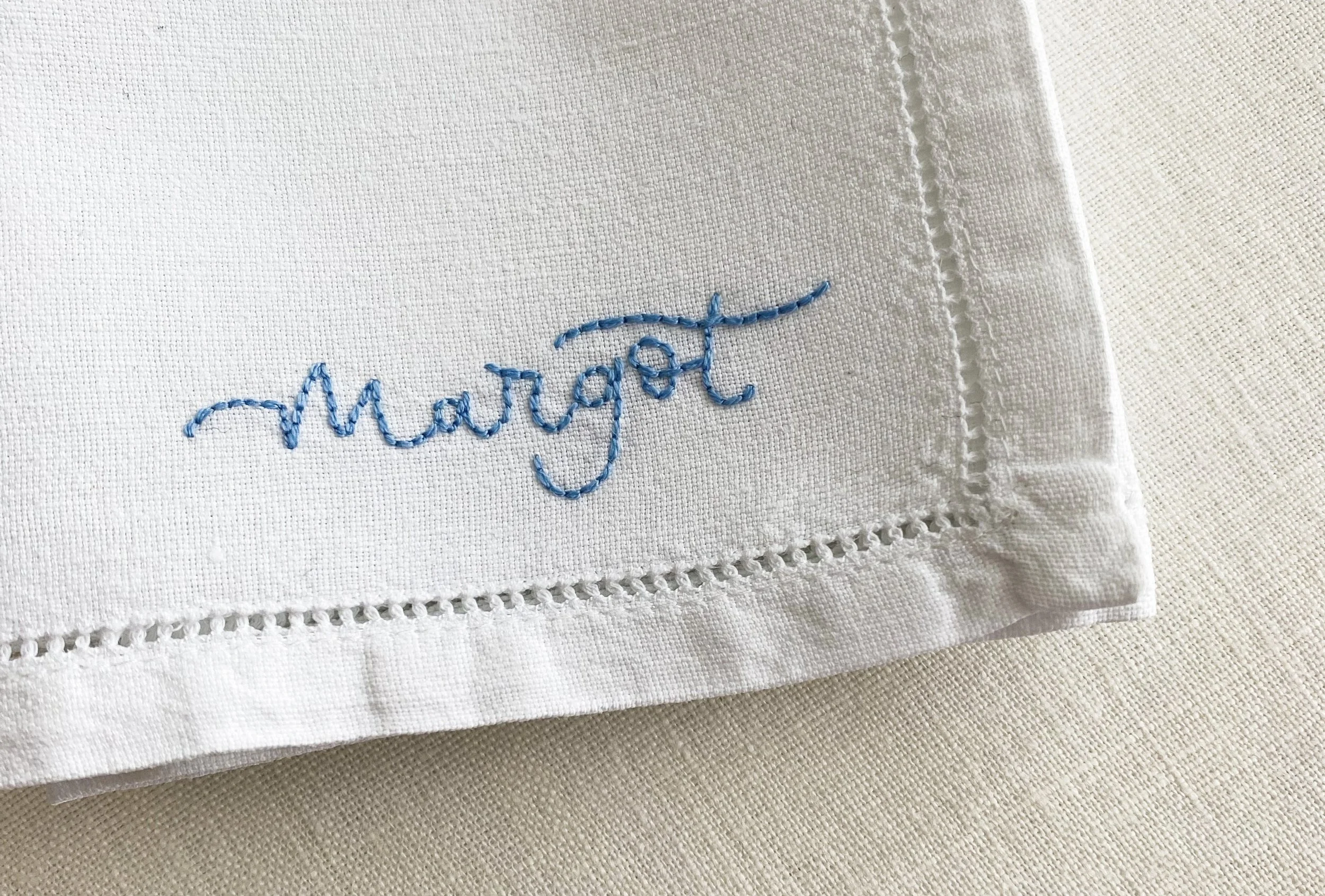 The edge of a napkin with the name embroidered in light blue backstitch.