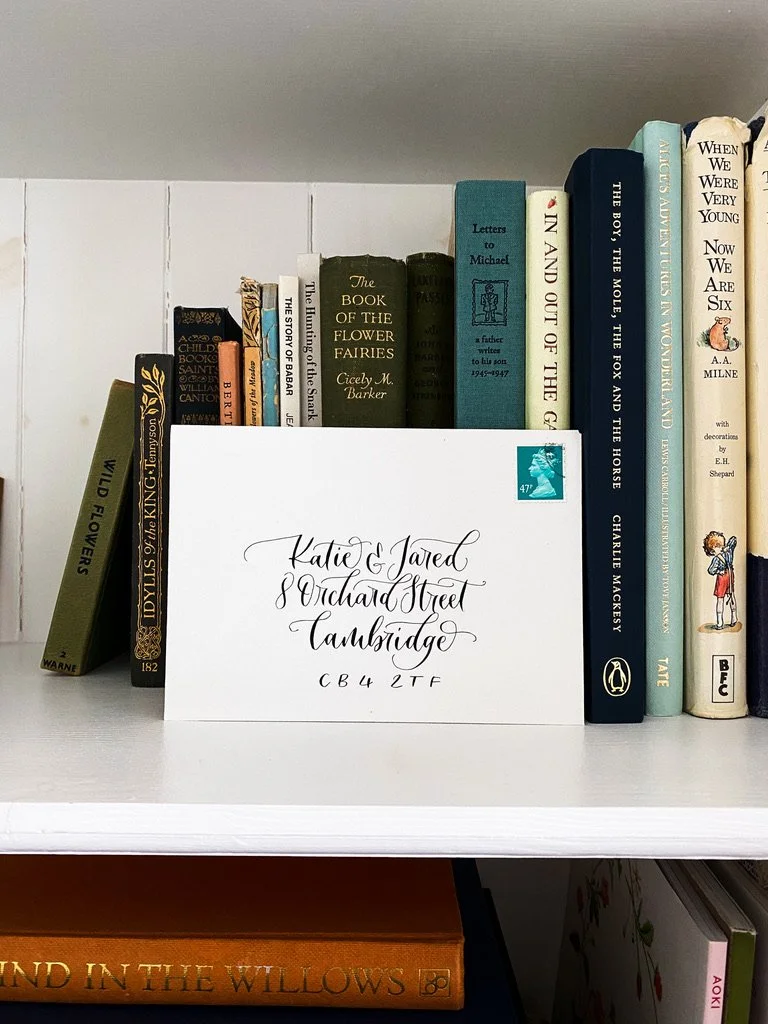 An envelope with the address written in modern calligraphy, sat on a shelf in front of hardback books