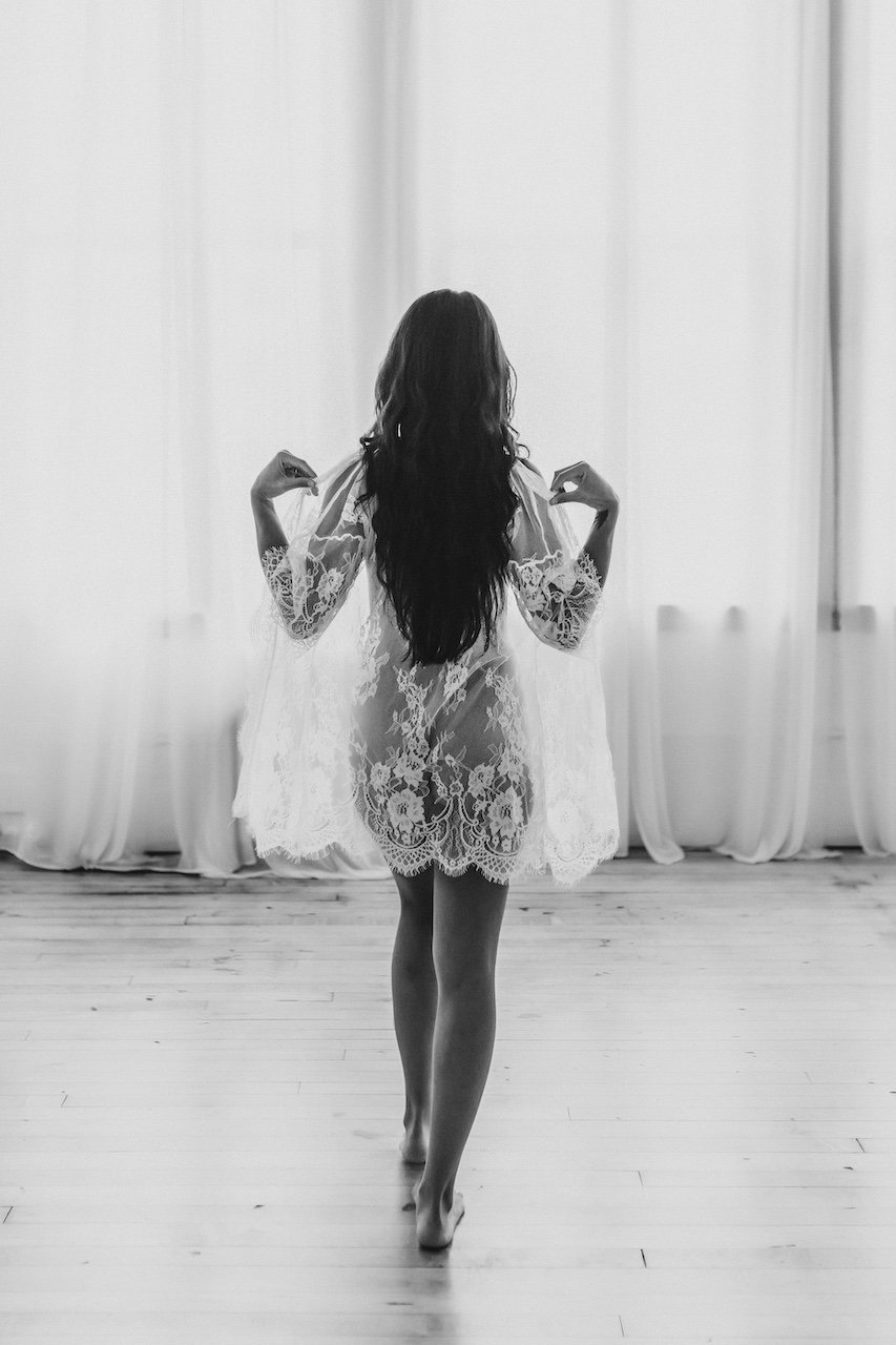 A female with long hair taking off her white lace robe in Ohio boudoir studio. 