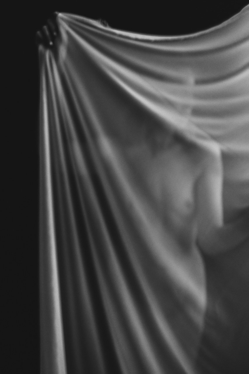 A woman covering her body with a sheer curtain in a photo studio.