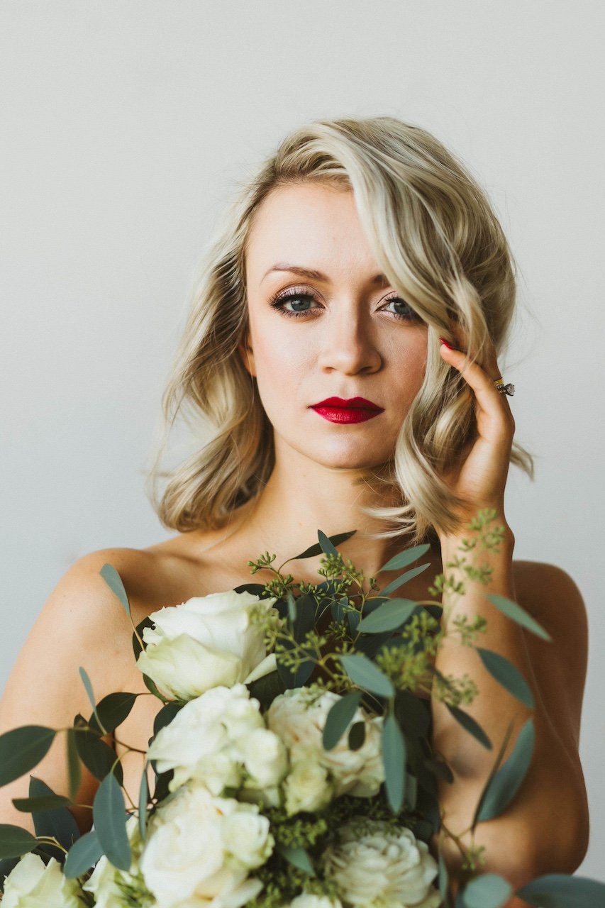 Girl in red lipstick holding bouquet of white flowers in glamour photography studio.