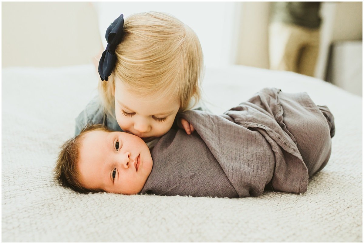 Big sister kissing newborn brother on the cheek for a lifestyle newborn picture. 