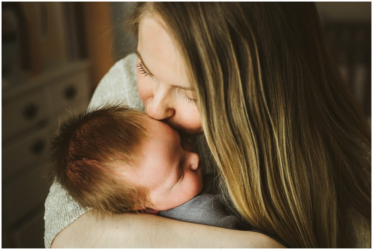 Mom kissing newborn son during a home lifestyle baby session. 