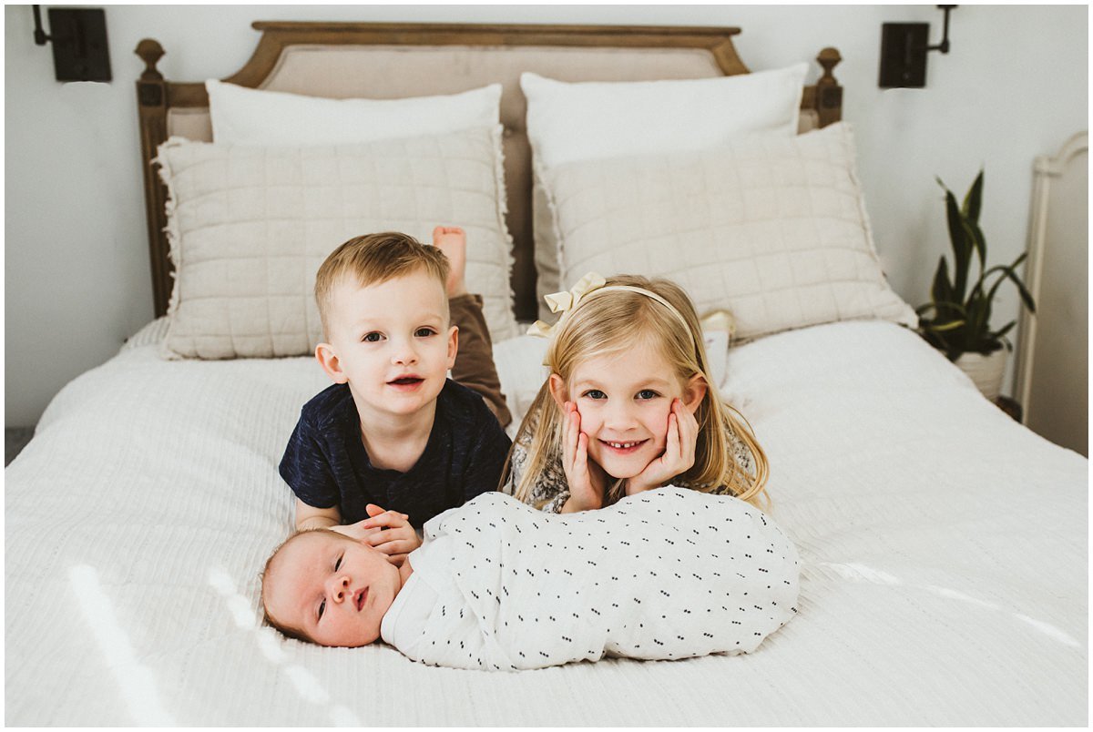 Two sibling with newborn brother on bedroom bed in Shaker Heights posing for pictures. 