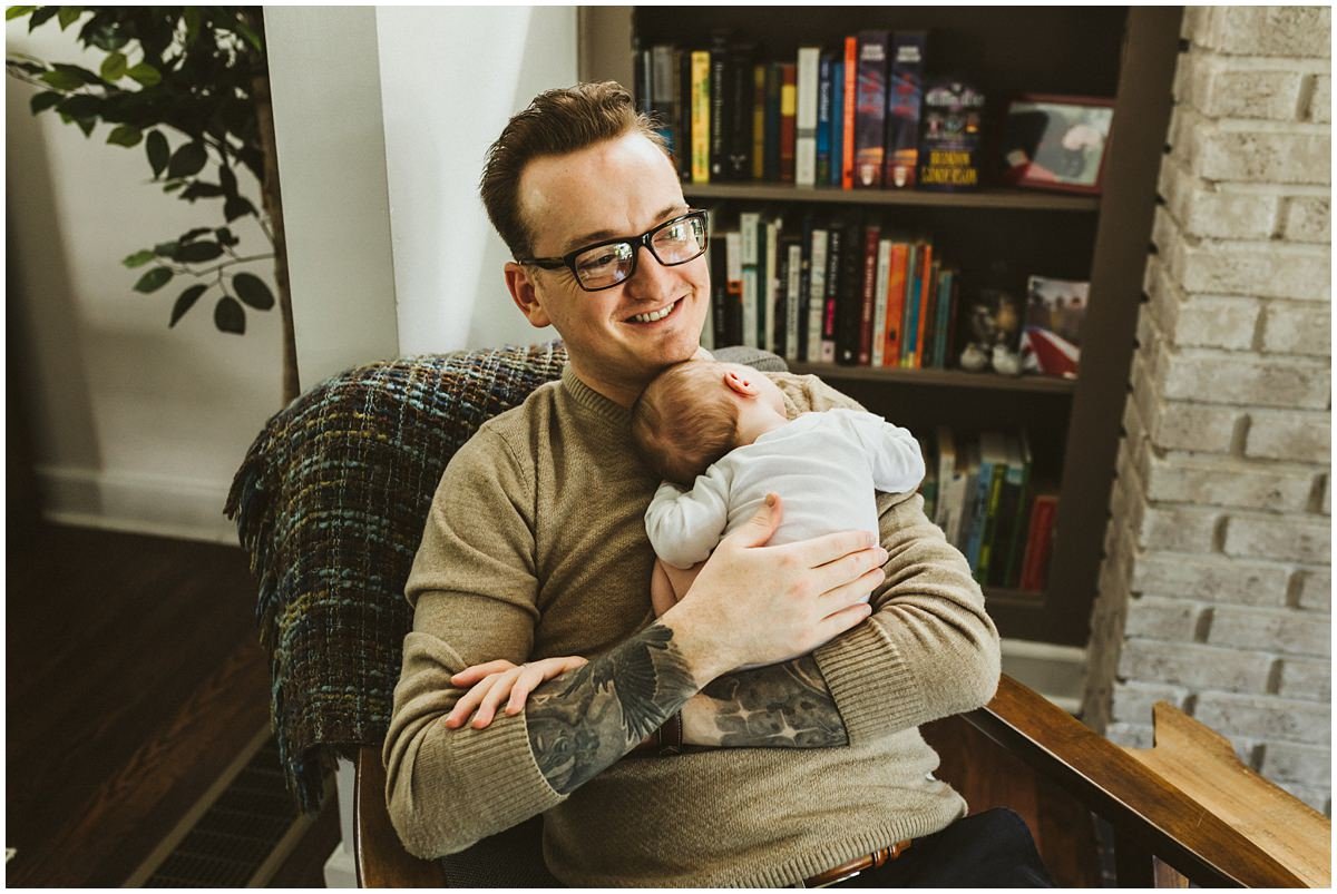 Dad sitting in lounge chair with newborn son in Cleveland Heights during lifestyle photos. 