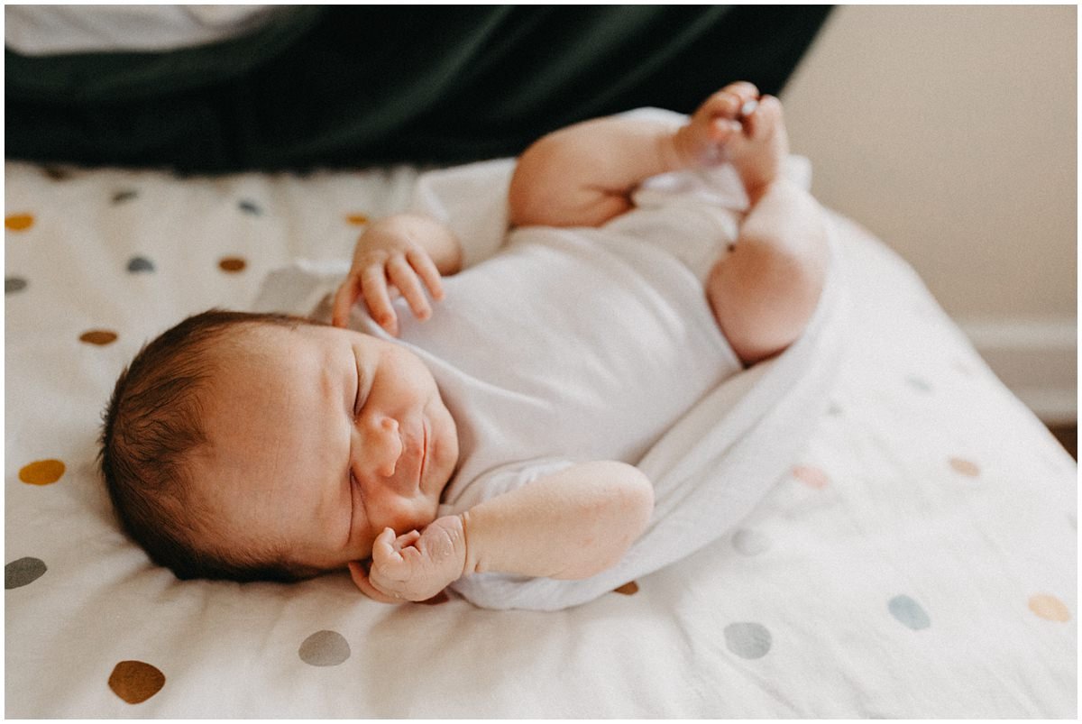 Newborn boy laying on polka dot sheets posing for in home photography.