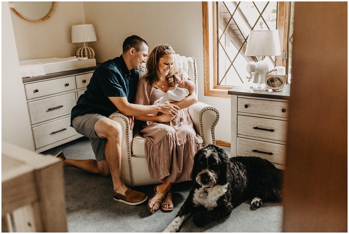 Parents in nursery with baby and dog posing for lifestyle in home pictures. 