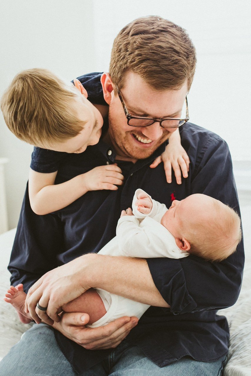 Dad and two brother snuggling on the bed during a newborn session in Cleveland, Ohio.