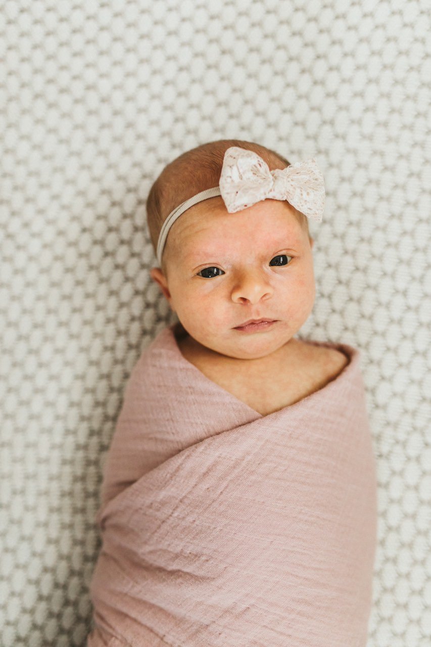 Infant daughter in swaddle posing for lifestyle newborn shoot. 