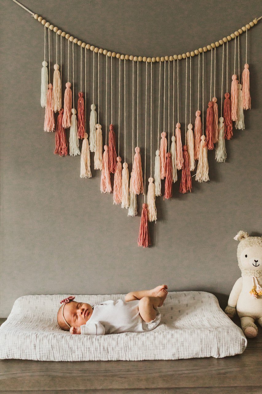 A baby girl laying on diaper changing station with wall art in nursery in Cleveland, Ohio.