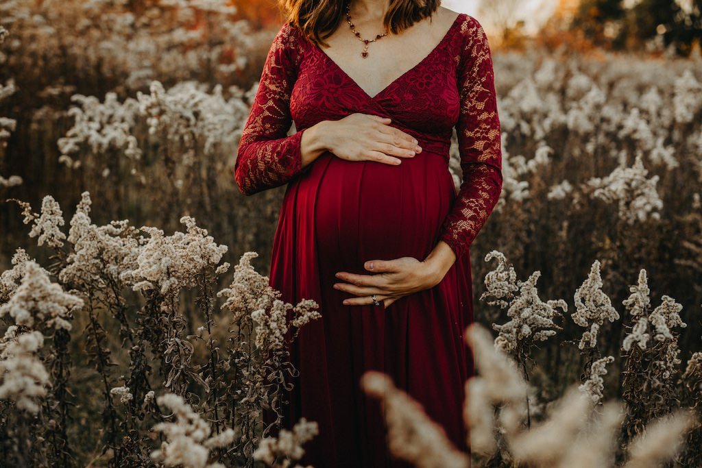 A pregnant woman in red gown posing for lifestyle maternity photo in Acacia Reservation Ohio.